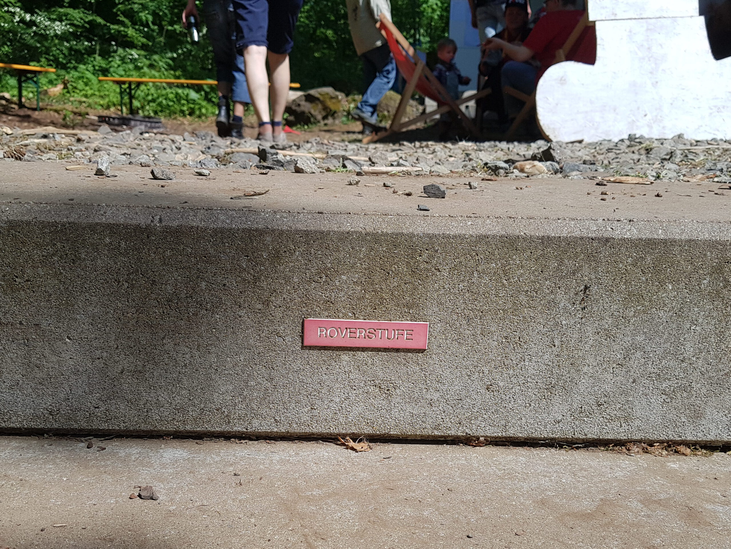 Eine Stufe aus Beton auf der eine rote Plakette mit der Aufschrift "Roverstufe" angebracht ist.